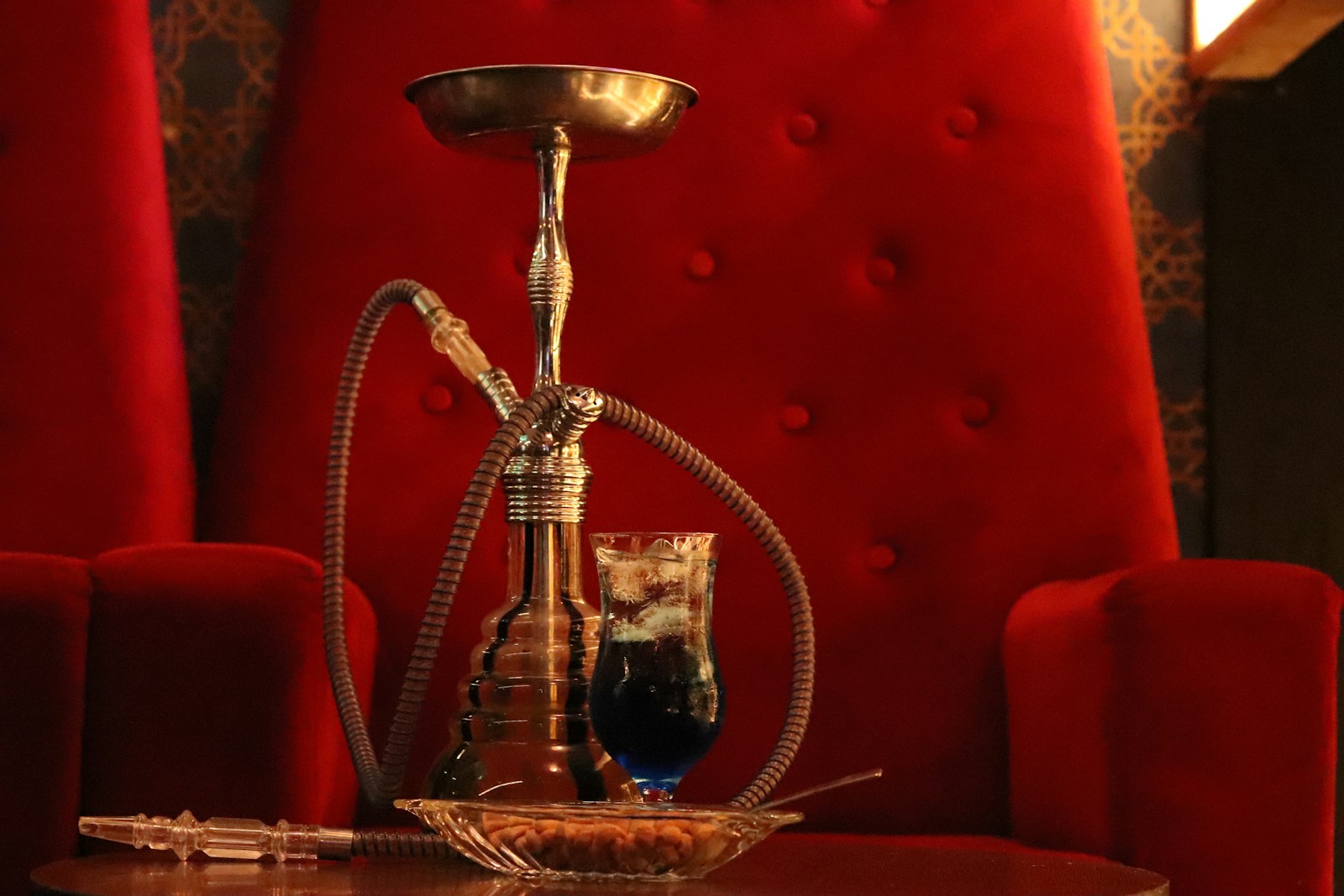 A hookah set up on a table beside a drink in a warm, low-lit lounge